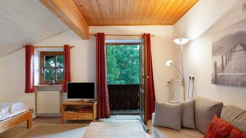 Une pièce confortable avec un plafond en bois, un lit, une télévision, un canapé et une fenêtre avec des rideaux.