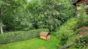 Eine Holzhütte mit geneigtem Dach, umgeben von dichtem Grün und einem gepflegten Rasen.