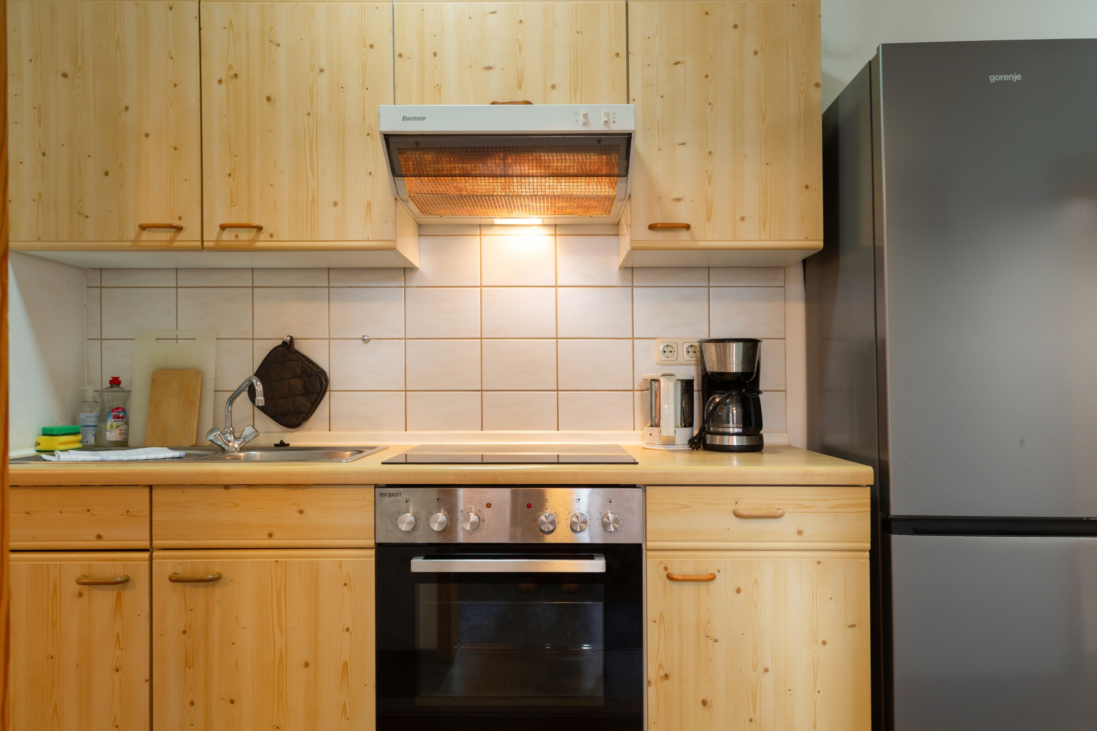 Een keuken met houten kastjes, een inbouwoven, een roestvrijstalen koelkast en een koffiezetapparaat.