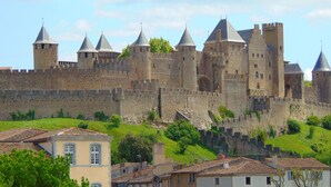 Un castell històric amb diverses torres i una muralla fortificada, envoltat de vegetació exuberanta i edificis tradicionals.