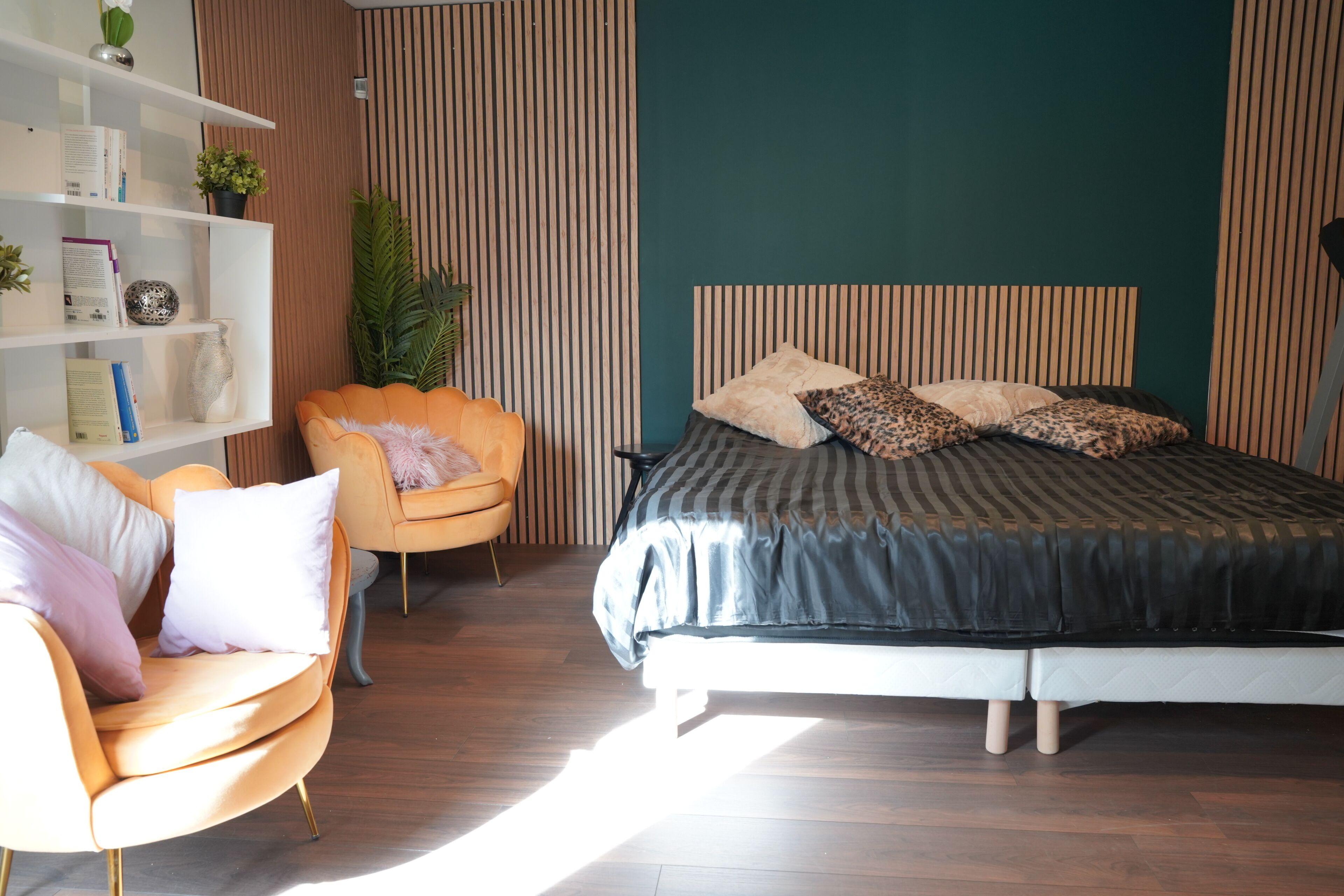 Een slaapkamer met een bed, een stoel, een boekenkast en een potplant.