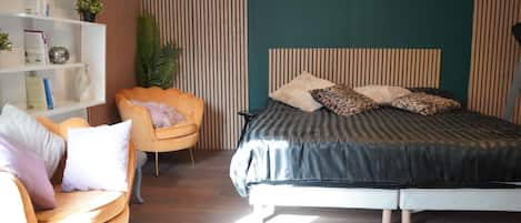 Ein Schlafzimmer mit einem Bett, einem Sessel, einem Bücherregal und einer Topfpflanze.