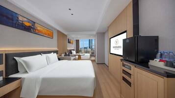 A modern hotel room with a large bed, a television, a desk, and a view of the city.