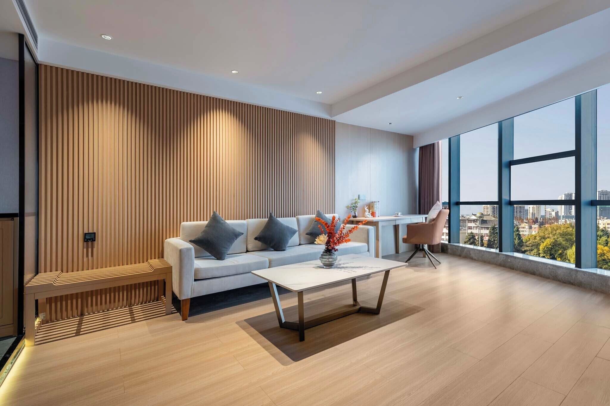 Un moderno salón con un sofá, una mesa de centro y una silla. Se ve una ventana grande con vistas a la ciudad.