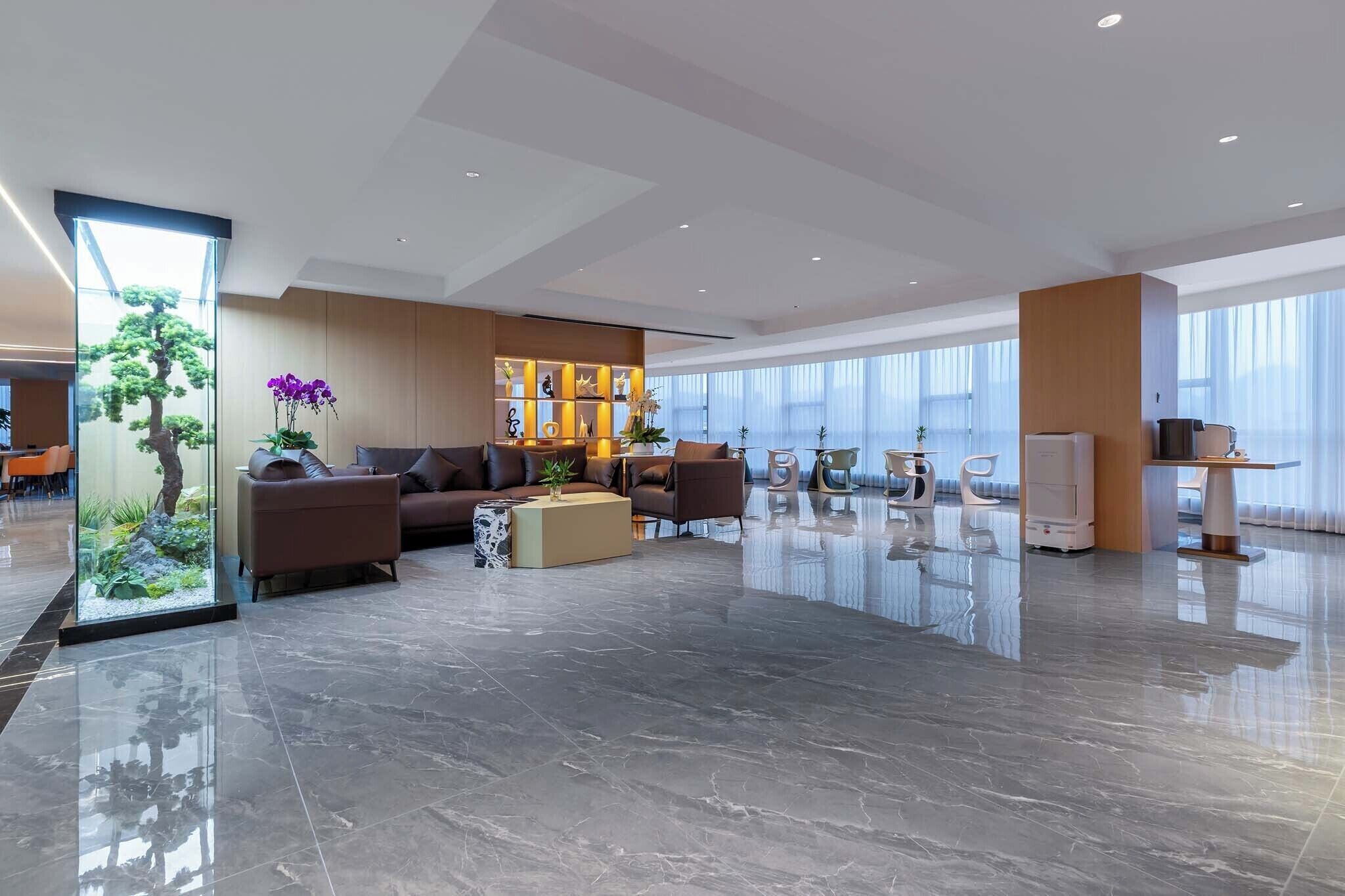 A modern hotel lobby with a seating area, a reception desk, and a large window providing natural light.