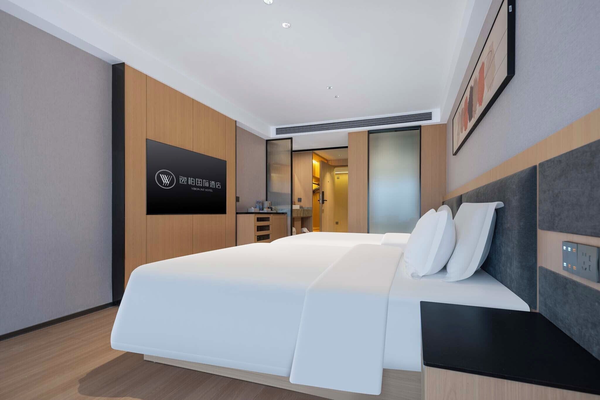 Habitación de hotel moderna con una cama grande, un armario, un escritorio y un baño visible a través de una puerta abierta.