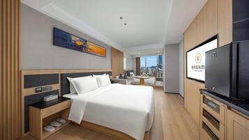 Habitación de hotel moderna con una cama grande, televisión de pantalla plana, escritorio con computadora y vista a la ciudad.