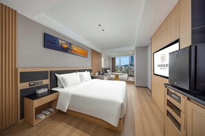 A modern hotel room with a large bed, a flat-screen TV, a desk with a computer, and a view of the city.