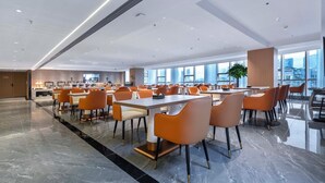 Un'ampia sala da pranzo con tavoli alti e sedie arancioni, grandi finestre con vista sulla città e un moderno design del soffitto.
