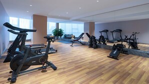 Una palestra moderna con diverse attrezzature cardio, un pavimento in legno e ampie finestre.