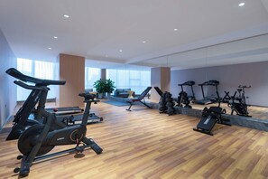 Uma academia moderna com diversos equipamentos de cardio, piso de madeira e amplas janelas.