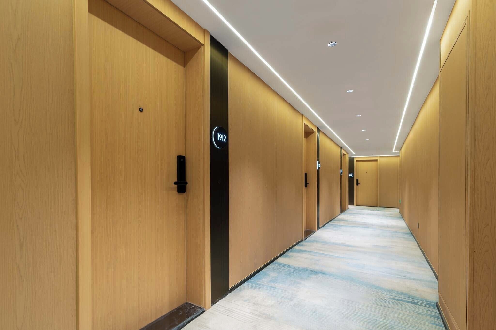 Un corridoio d'albergo con porte in legno, numeri civici sulle porte e una moquette decorata.