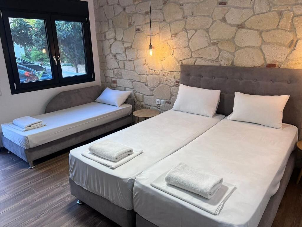 A bedroom with two beds, a stone wall, a window with a view, and a bedside lamp.