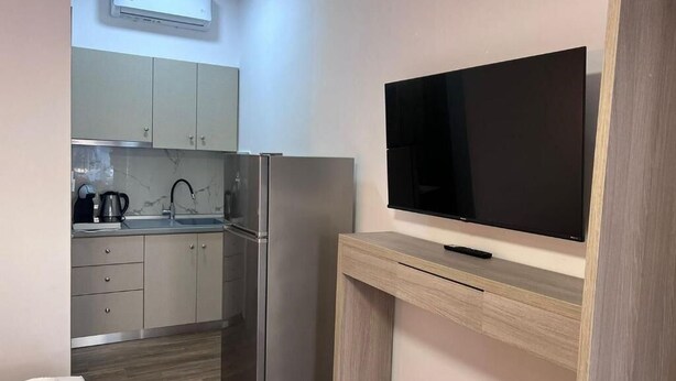 A compact kitchen with a refrigerator, a coffee maker, and a flat-screen TV on a wooden stand. - Naria Studios  (Kassandra)