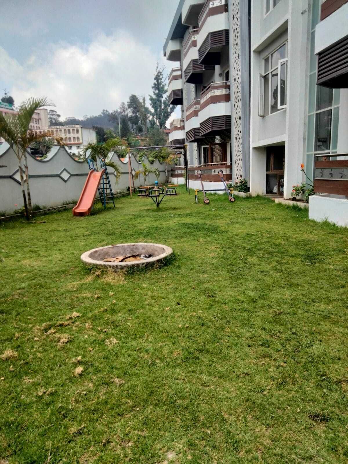 A grassy courtyard with a slide, a fire pit, and a building with balconies.