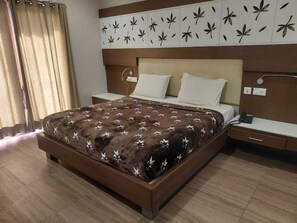 Quarto de hotel com uma cama grande, mesa de cabeceira e parede com padrão de folhas.
