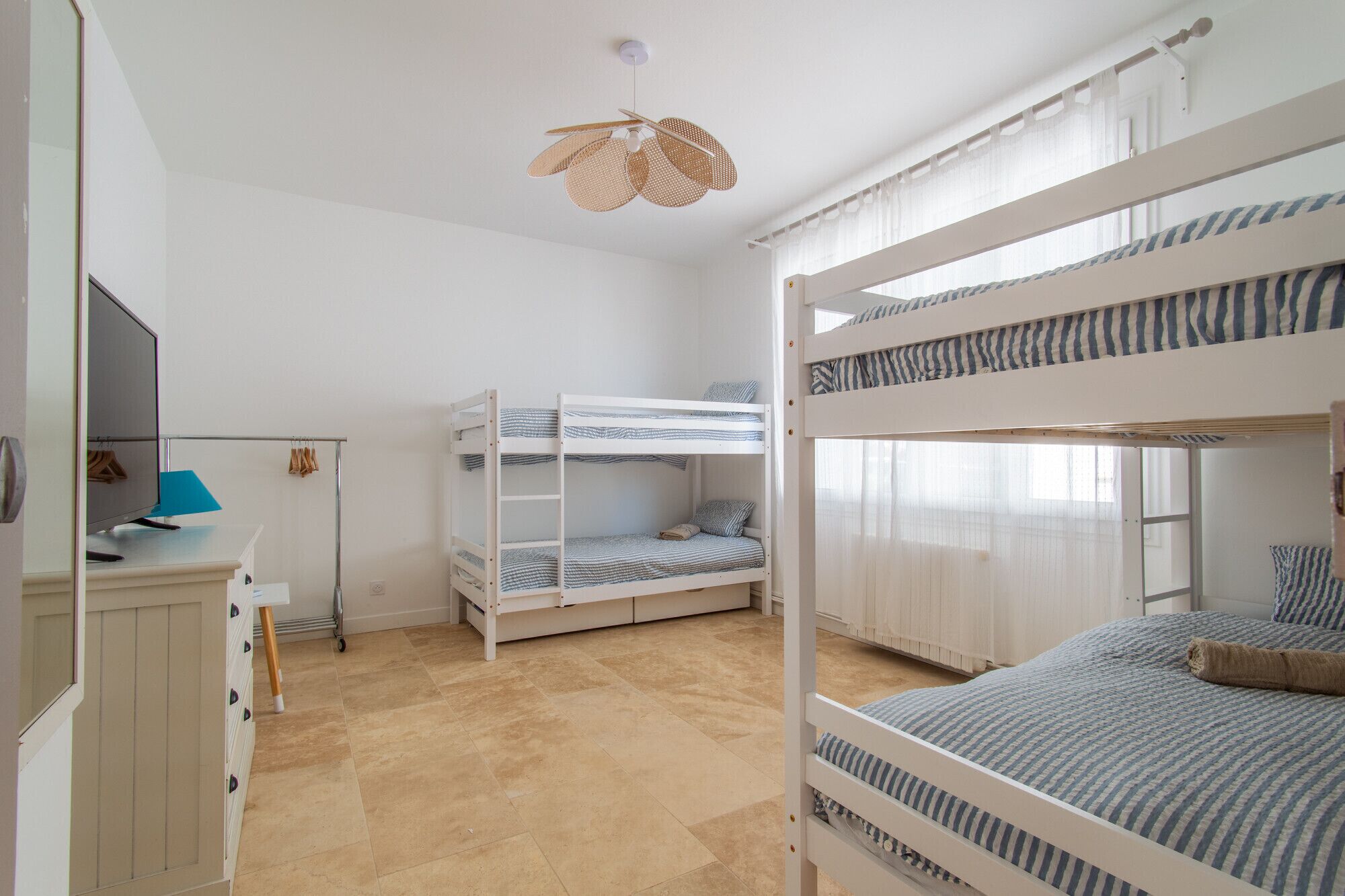 A room with bunk beds, a desk with a computer, and a hanging light fixture.