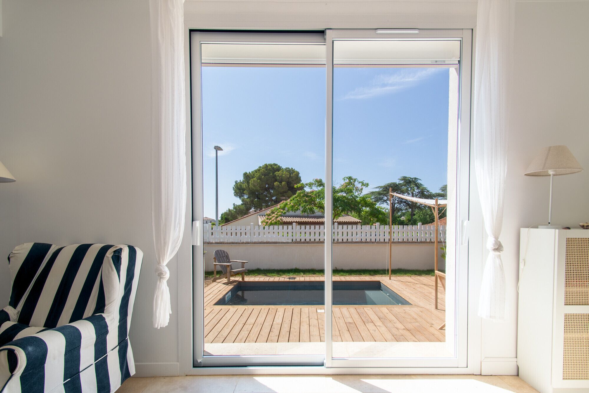 Une pièce dotée d’une porte-fenêtre coulissante donnant sur un espace extérieur avec une terrasse en bois et une piscine.