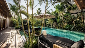 A poolside area with a wooden deck, lounge chairs, and tropical plants.