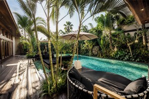 A poolside area with a wooden deck, lounge chairs, and tropical plants. - Villa NA by GORO (Badung)