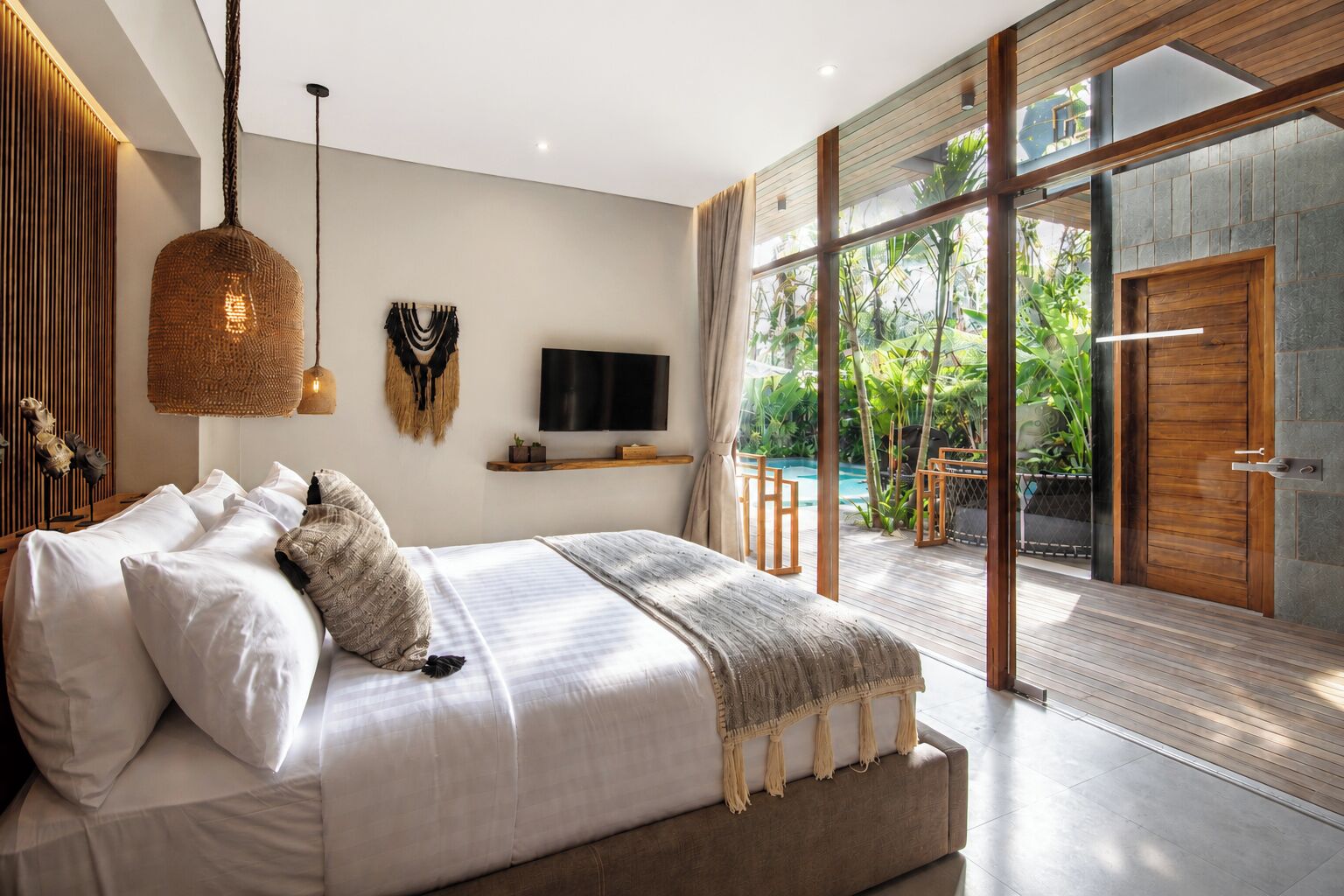 A modern bedroom with a large bed, a television, and a view of a swimming pool.