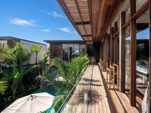 A wooden deck with a pool, surrounded by tropical plants and a modern building with large windows. - Villa NA by GORO (Badung)