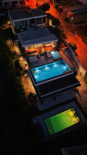 Et moderne hus med swimmingpool, udendørs møbler og en veloplyst terrasse.