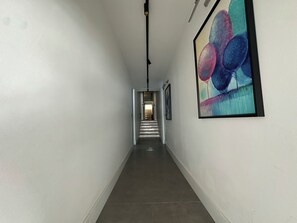 En gang med trappe op til en anden etage, et abstrakt billede i ramme på væggen, og en lampe i loftet.