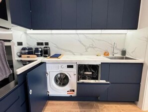 Eine kompakte Küche mit Waschmaschine, Kaffeemaschine und Spüle.
