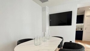 Un comedor moderno con una mesa de mármol, sillas negras y un televisor de pantalla plana montado en la pared.