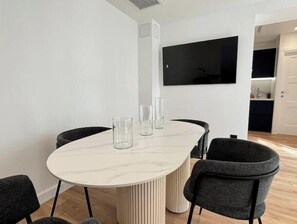 Ein moderner Essbereich mit einem Marmortisch, schwarzen Stühlen und einem an der Wand montierten Flachbildfernseher.