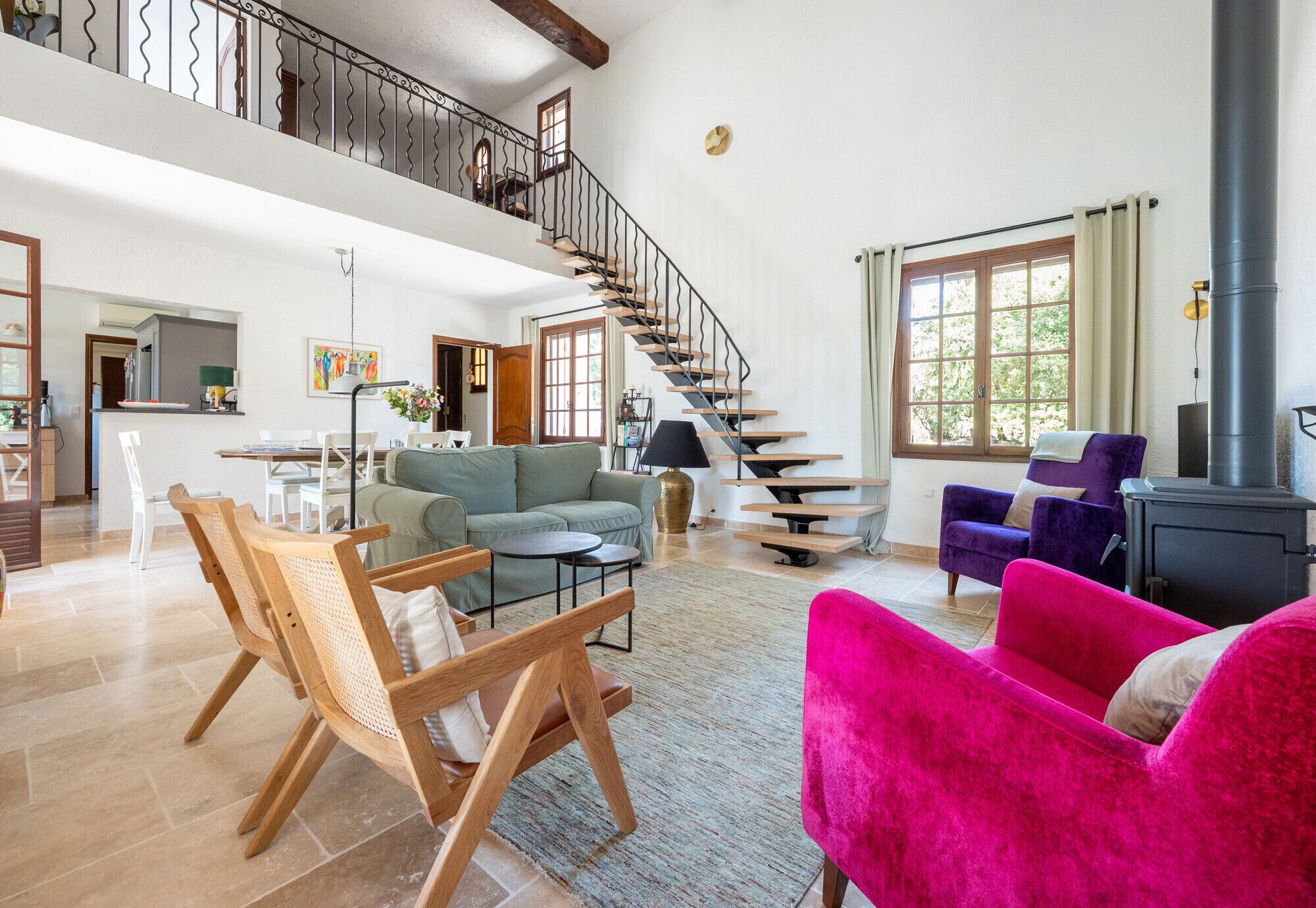 A spacious living area with a high ceiling, a staircase, a fireplace, and a dining area.
