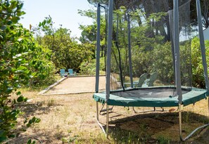 A trampoline with a safety net, surrounded by trees and shrubs, with two blue chairs in the background. - Villa Parete Vidauban | Luxury villa with pool and large garden (Vidauban)
