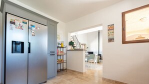 Uma cozinha moderna com geladeira de aço inoxidável, dispenser de água e área de refeições com mesa e cadeiras.