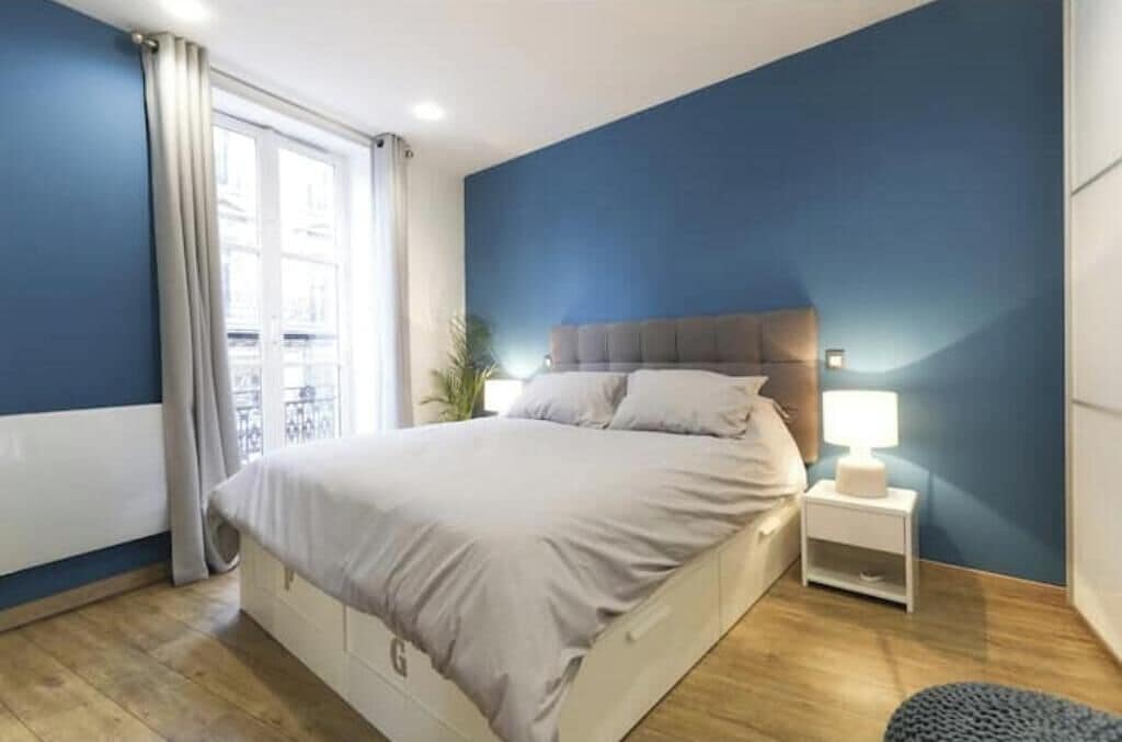 A bedroom with a bed, bedside table, and a view of a balcony.