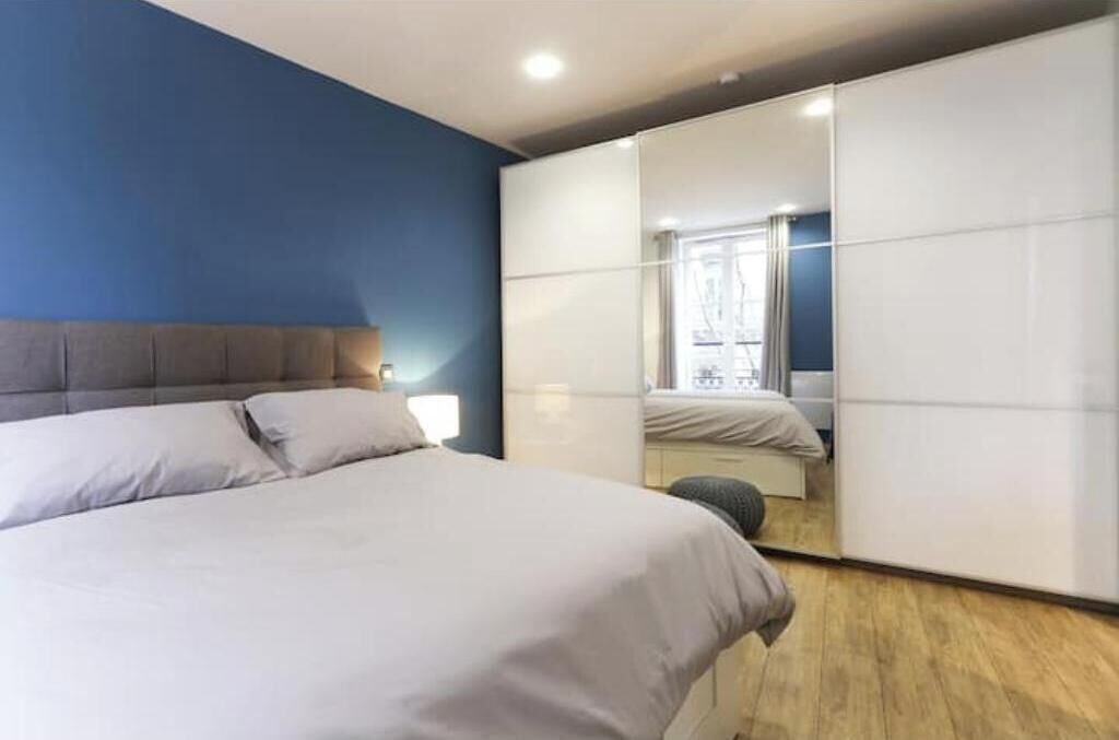 A bedroom with a bed, a wardrobe, and a mirror reflecting another room.