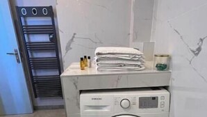 A compact, modern laundry area with a front-loading washing machine, a drying rack, and a neatly stacked pile of folded towels. - Spacious, recently renovated apartment near the Louvre (Île-de-France)