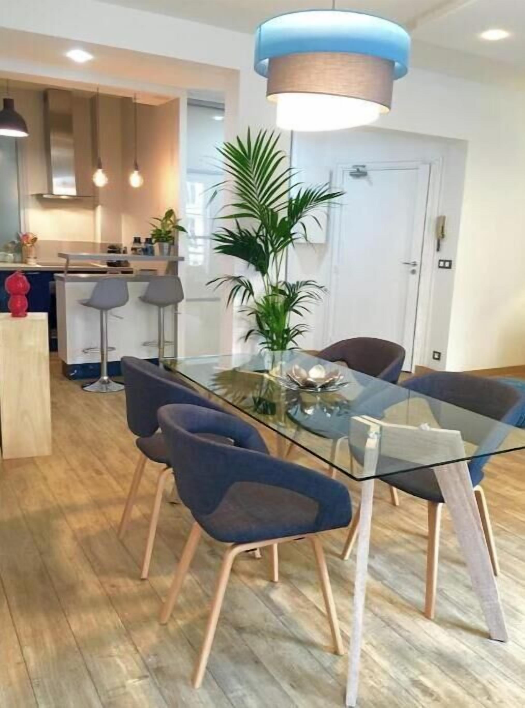 A modern dining area with a glass table, blue chairs, and a hanging light fixture.