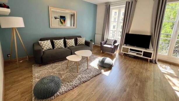A living room with a sofa, two side tables, a television, and a large window with curtains. - Spacious, recently renovated apartment near the Louvre (Île-de-France)