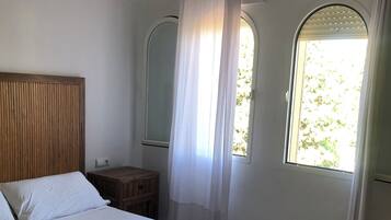 A bedroom with a bed, a bedside table, a hanging light fixture, and a window with curtains.