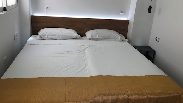 Una habitación de hotel con una cama, ropa de cama blanca, un cabecero de madera y una mesita de noche.