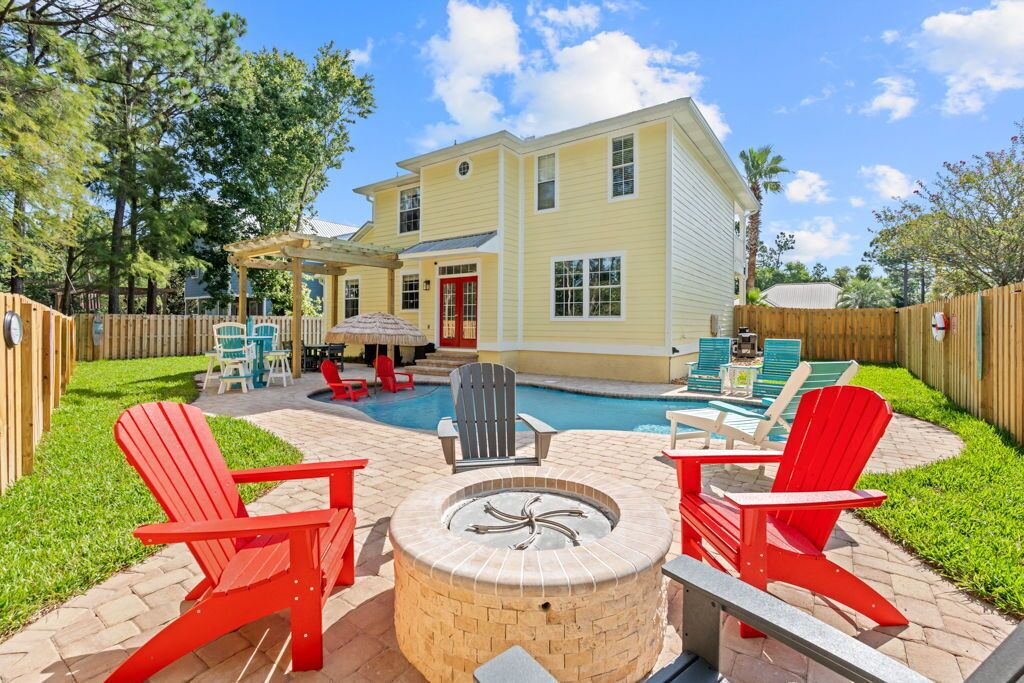 A backyard with a pool, outdoor seating, and a house.