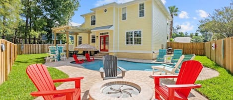 A backyard with a pool, outdoor seating, and a house.