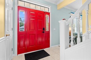 A red door with a white frame, a black doormat, and a staircase with white balusters. - The Love Bug: Private Pool, Golf Cart & Fire Pit, Sleeps 16 & Pet Friendly (Panama City Beach)