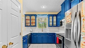 Eine Küche mit blauen Schränken, einem Edelstahl-Kühlschrank und einem Fenster mit Blick ins Grüne.