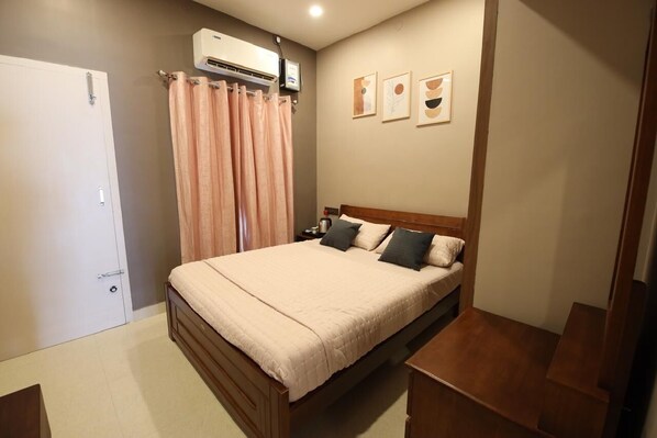 A bedroom with a bed, a nightstand, a wooden bench, a door, and an air conditioning unit.