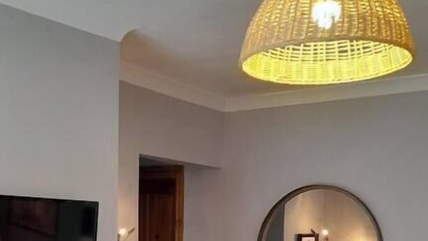 A living room with a fireplace, a green armchair, a television, a hanging light fixture, and a round mirror on the wall. - #06 Riverside Retreat| Near the NEC| Guest for 6 (Coleshill)
