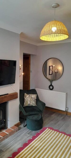 A living room with a fireplace, a green armchair, a television, a hanging light fixture, and a round mirror on the wall. - #06 Riverside Retreat| Near the NEC| Guest for 6 (Coleshill)