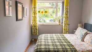A bedroom with a bed, a window with curtains, a bedside table with a lamp, and framed pictures on the wall. - #06 Riverside Retreat| Near the NEC| Guest for 6 (Coleshill)