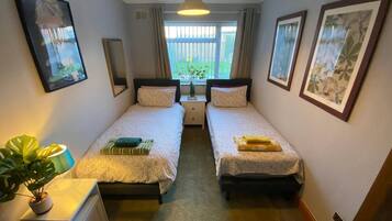 A room with two beds, a bedside table, a potted plant, and a window with curtains.
